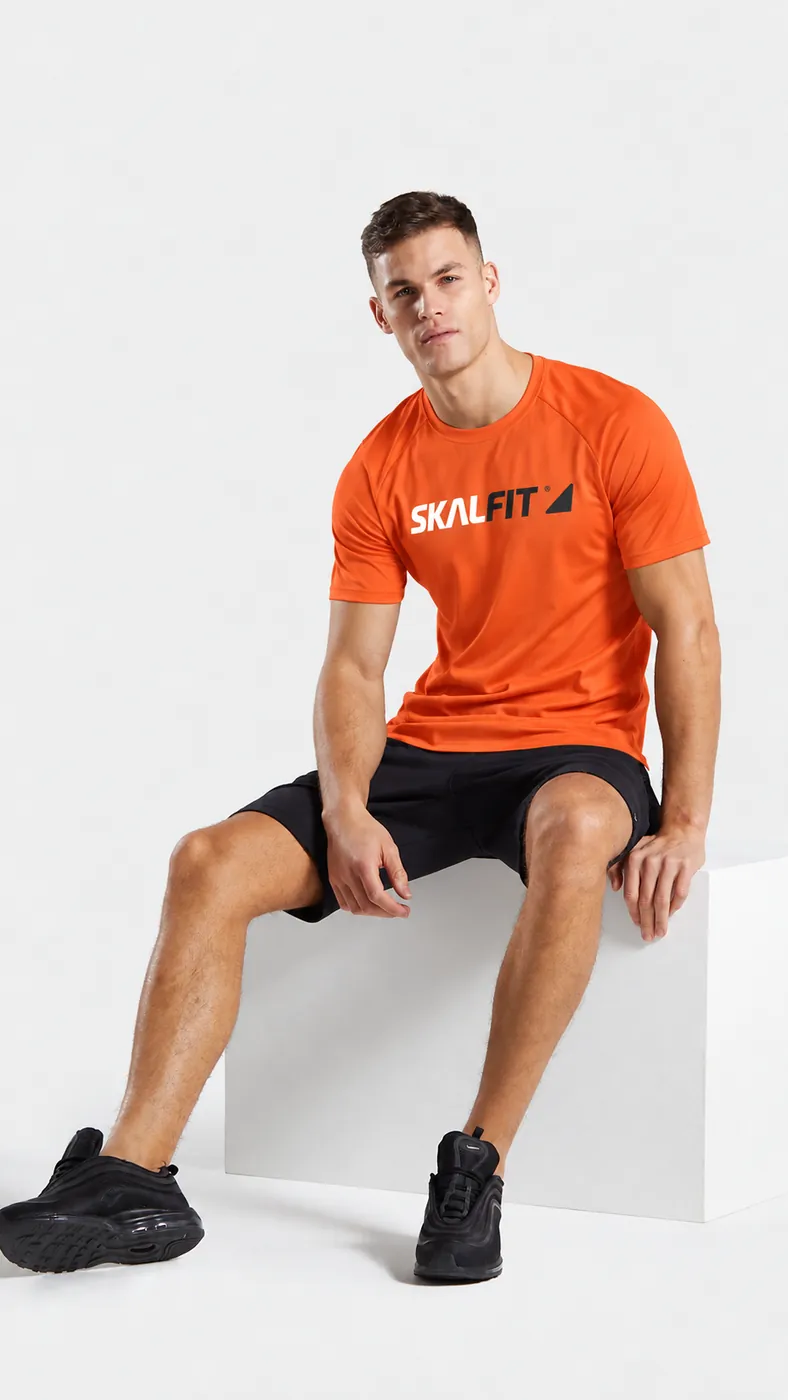 Homem sentado com camiseta dry fit laranja personalizada com a logo da Skalfit