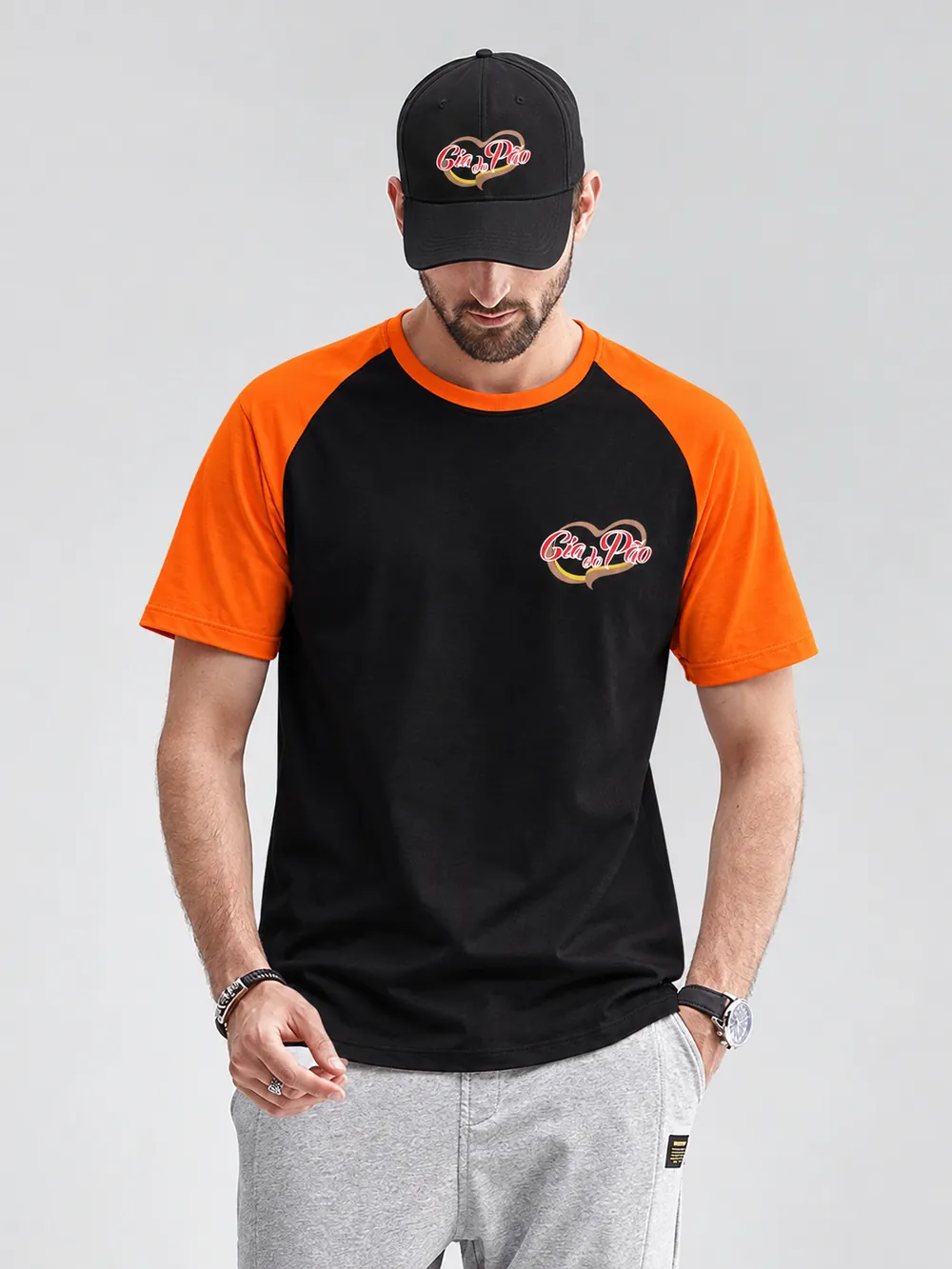 Homem com camiseta raglan preta e laranja e boné preto, ambos com a logo da padaria Cia do Pão